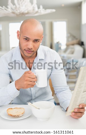 Portrait of a serious young man drinking coffee while reading newspaper at home