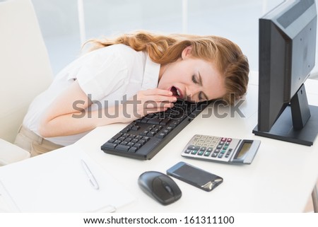 Young businesswoman resting head on keyboard while yawning in the office
