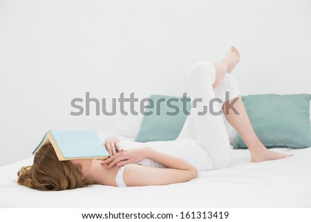 Side view of a young woman with book over face resting in bed at home