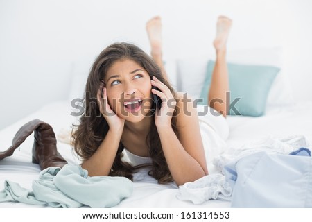 Young woman using mobile phone as she looks up in bed at home