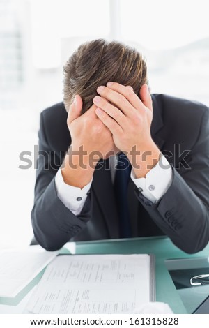 Worried young businessman sitting with head in hands at office desk