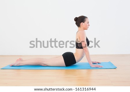 Full length side view of a fit young woman doing the cobra pose in fitness studio