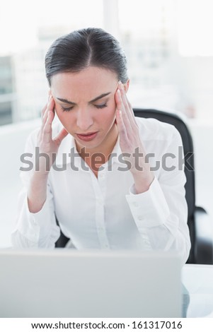 Young businesswoman suffering from headache in front of laptop at office desk