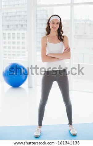 Portrait of a toned young woman with hands folded standing in fitness studio