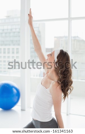 Side view a fit young woman stretching hand in a bright fitness studio