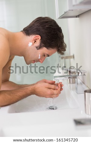 Side view of a shirtless young man washing face in the bathroom