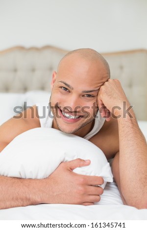 Portrait of a smiling casual bald young man lying in bed at home