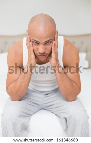 Portrait of a young bald man suffering from headache in bed at home