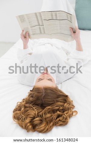 Overhead view of a pretty young blond reading newspaper while resting in bed at home