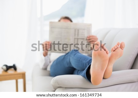 Full length of a relaxed man reading newspaper on sofa in a bright house