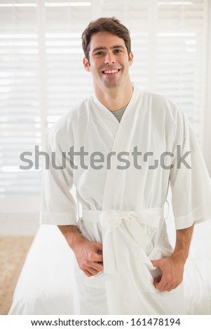 Portrait of a young smiling man in bathrobe standing in bedroom at home