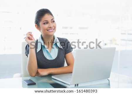 Thoughtful businesswoman looking away while using laptop on desk in a bright office