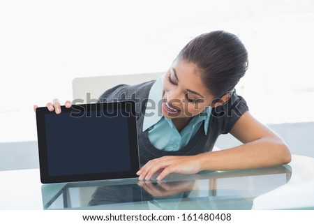 Smiling young businesswoman displaying tablet PC on desk in a bright office
