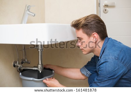 Side view of a handsome plumber repairing the drain of sink in bathroom