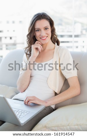 Portrait of a casual young woman using laptop on sofa in a bright house