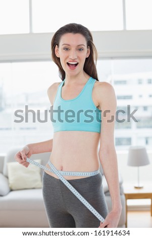 Portrait of a shocked toned young woman in sportswear measuring waist in fitness studio