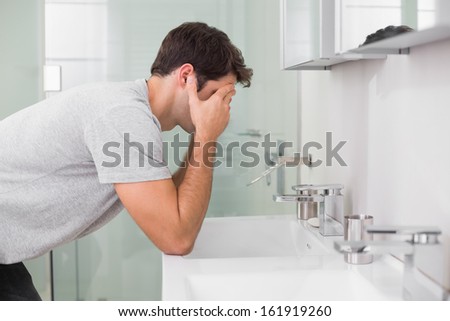 Side view of a young man with head in hands at washbasin in bathroom