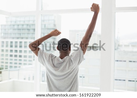 Rear view of a young Afro man stretching his arms near window at home
