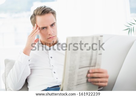 Portrait of a serious relaxed man reading newspaper on sofa in a bright house