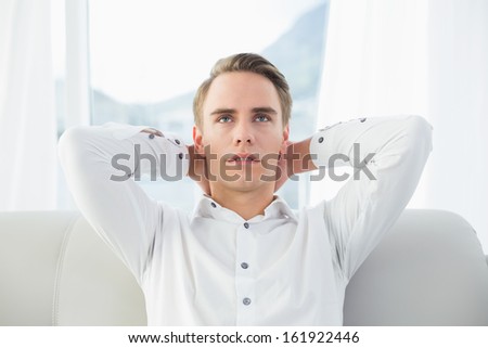 Close up of a thoughtful relaxed young man sitting on sofa in a bright house