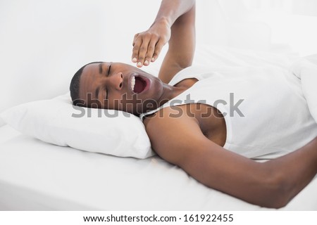Young sleepy Afro man yawning in bed at home