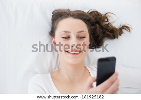 High angle view of a young brunette looking at mobile phone in bed at home