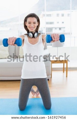 Portrait of a fit young woman exercising with dumbbells in bright fitness studio