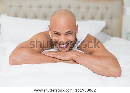 Portrait of a smiling casual bald young man lying in bed at home