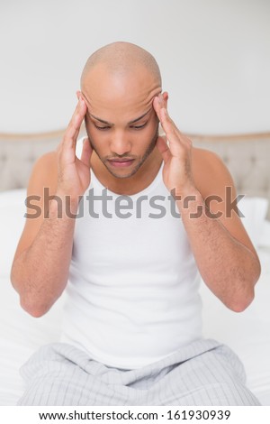 Young bald man suffering from headache in bed at home