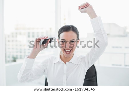 Cheerful elegant businesswoman cheering with hands raised at office