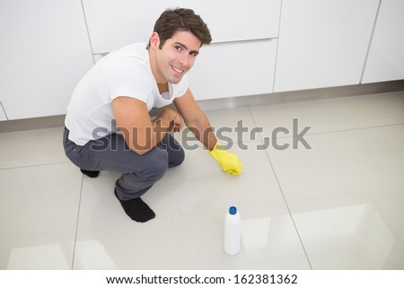Portrait of a smiling young man cleaning the kitchen floor at house