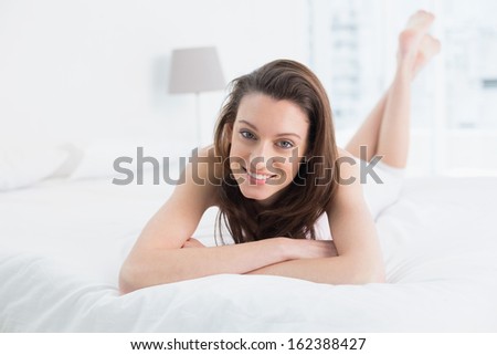 Full length portrait of a smiling young woman resting in bed at home