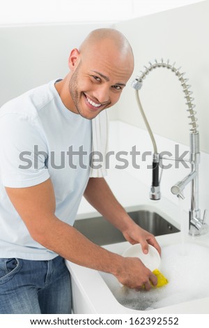 Portrait of a smiling young man doing the dishes at kitchen sink in the house