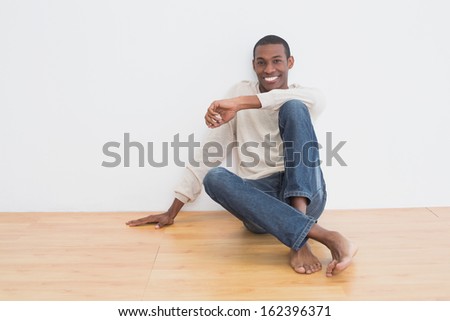 Full length portrait of a casual Afro young man sitting on floor in an empty room
