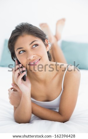Thoughtful young woman using mobile phone in bed at home