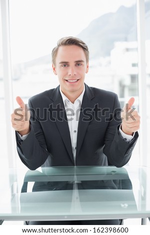 Portrait of a smiling young businessman gesturing thumbs up at office desk