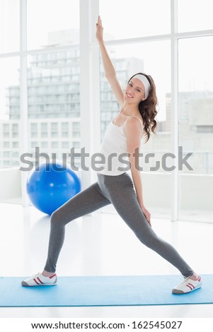 Full length portrait a fit young woman stretching hand in a bright fitness studio