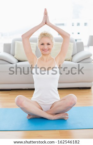 Full length portrait of a toned young woman sitting with joined hands over head at fitness studio