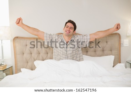 Young Man Waking Up In Bed And Stretching His Arms At Home