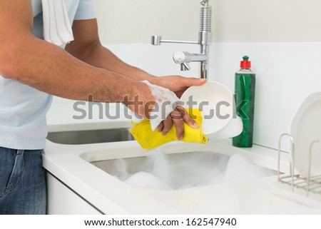 Close up mid section of a man doing the dishes at kitchen sink in the house
