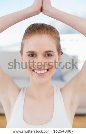 Close up portrait of a smiling young woman with joined hands over head at fitness studio