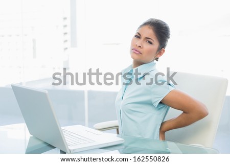 Young businesswoman suffering from back ache in front of laptop in the office