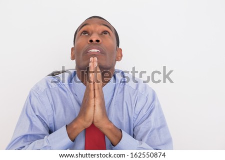 Close up of a serious young Afro businessman looking up with joined hands against white background