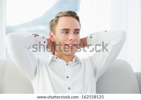 Smiling relaxed young man sitting on sofa in a bright house