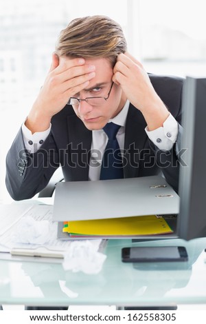 Portrait of a worried businessman with documents in front of computer at office desk
