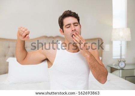 Young man waking up in bed and stretching his arms at home