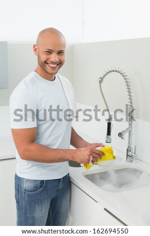 Portrait of a smiling young man doing the dishes at kitchen sink in the house