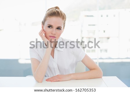 Thoughtful businesswoman looking away while sitting at desk in a bright office
