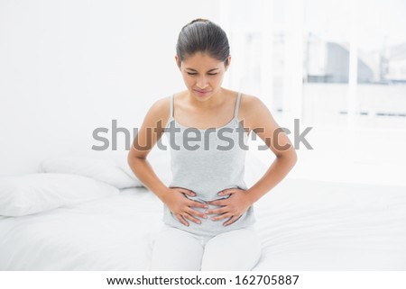 Casual young woman with stomach pain sitting in bed at home