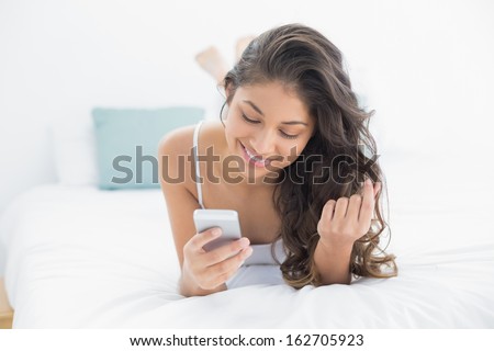 Smiling young woman looking at mobile phone in bed at home